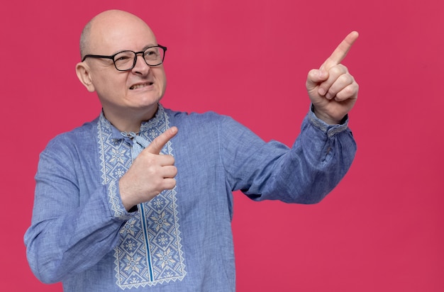 Homme slave adulte souriant en chemise bleue portant des lunettes optiques regardant et pointant sur le côté