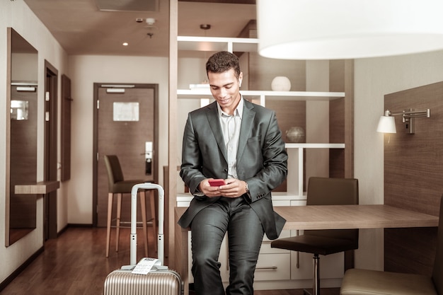 Homme avec smartphone. Jeune homme aux cheveux noirs lisant ses lettres d'affaires sur un smartphone rouge