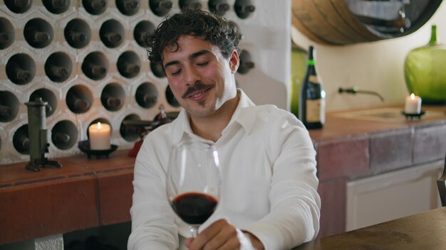 Photo homme sommelier mélangeant du vin dans un verre évaluant la couleur assis restaurant gros plan