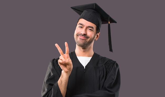 Homme sur son jour de remise des diplômes Université heureux et comptant deux avec les doigts sur fond violet