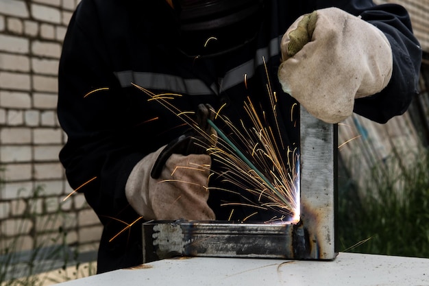 Photo un homme soudeur avec des gants de construction et un masque de soudage est soudé avec une machine à souder en métal à l'extérieur