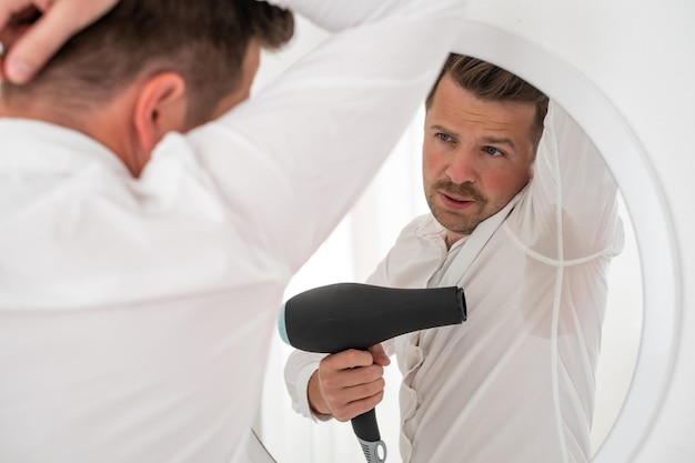 Homme souffrant d'hyperhidrose transpirant très fort sous l'aisselle essayant de sécher avec un ventilateur