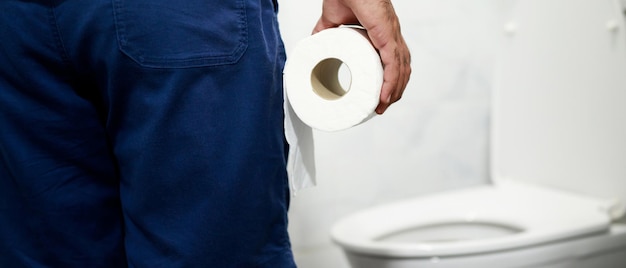 L'homme souffre de diarrhée main tenir un rouleau de papier de soie devant la cuvette des toilettes constipation dans la salle de bain traitement des douleurs à l'estomac et des soins de santé d'hygiène