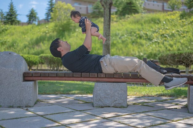 Un homme soulève un bébé sur un banc dans un parc.