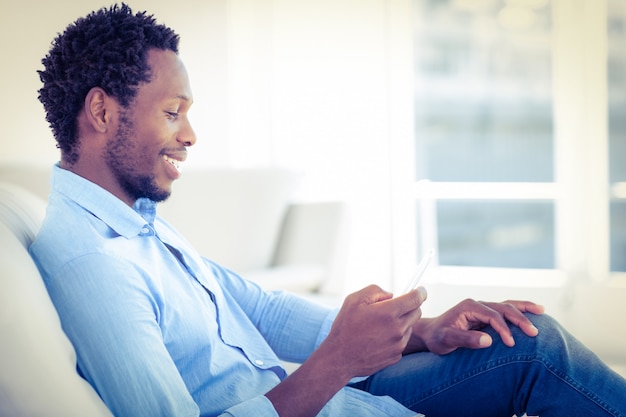 Homme souriant à l&#39;aide de téléphone portable tout en étant assis sur le canapé à la maison