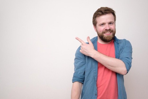 Un homme souriant et amical montre son doigt sur un mur blanc avec espace de copie