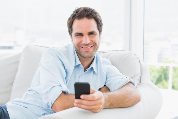 Homme souriant assis sur le canapé en envoyant un texte