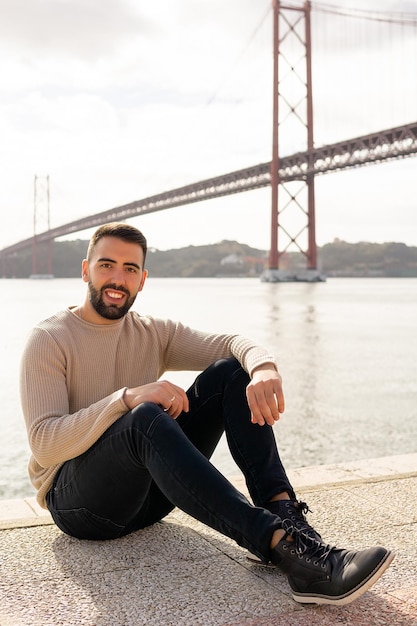 Homme souriant assis avec le pont du 25 avril en arrière-plan à Lisbonne