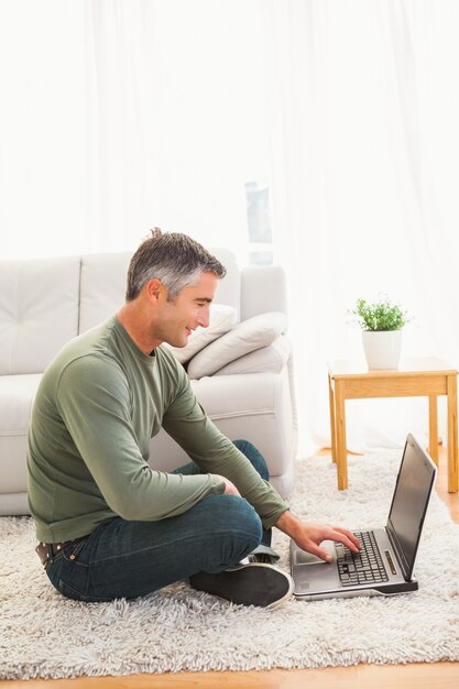 Homme souriant, assis sur un tapis en utilisant un ordinateur portable