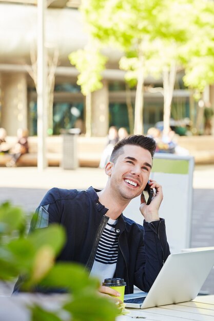 Homme souriant au téléphone au café avec ordinateur portable