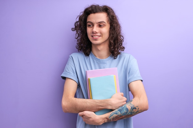 Homme souriant aux longs cheveux bouclés tenant des livres dans les mains, allant à l'université