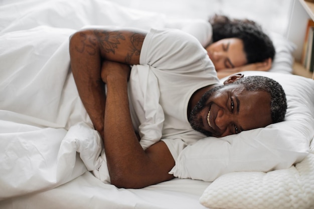 Homme souriant à la caméra pendant que la femme dort dans son lit