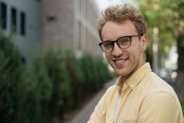 Homme souriant confiant portant des lunettes élégantes regardant la caméra debout dans la rue