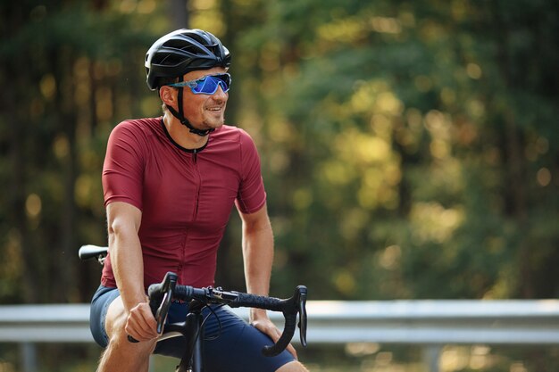 Homme souriant dans un casque de protection, des lunettes en miroir et des vêtements de sport profitant de la belle nature tout en faisant du vélo à l'extérieur