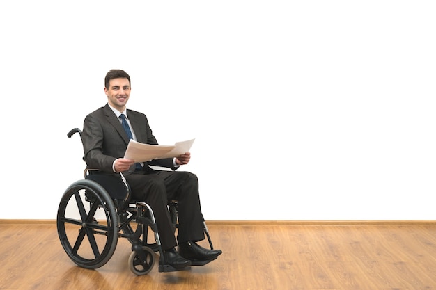 L'homme souriant dans le fauteuil roulant tenant des papiers sur le fond du mur blanc