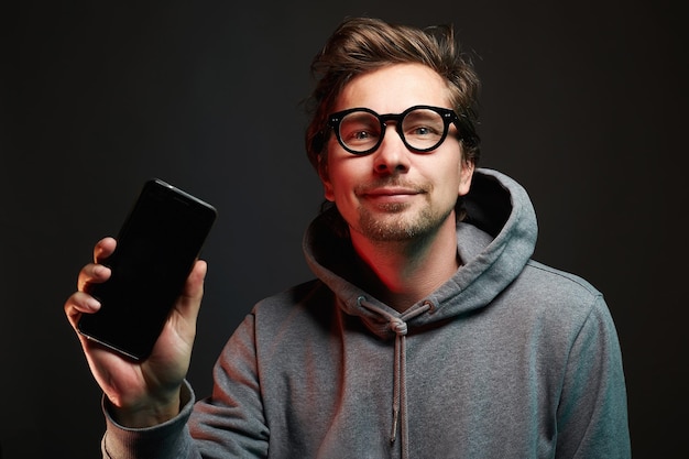 Homme souriant dans des verres Heureux mec tenant et montrant son smartphone