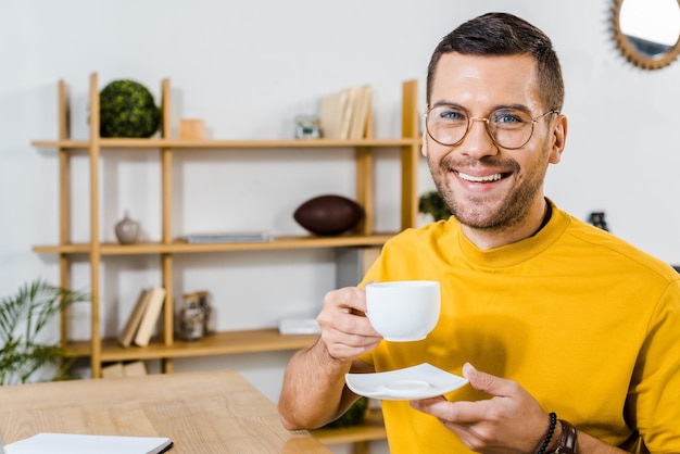 Homme souriant dans des verres tenant une tasse avec du café à la maison