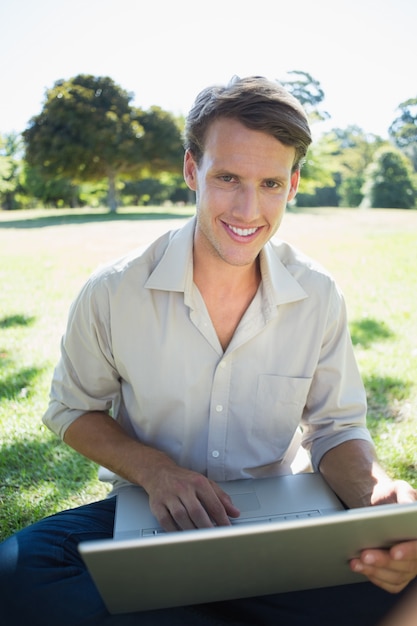 Homme souriant élégant en utilisant son ordinateur portable dans le parc