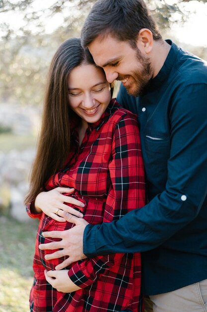 Un homme souriant embrasse une femme enceinte par derrière en gros plan