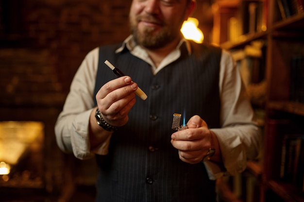 Un homme souriant fume une cigarette avec un embout buccal, une étagère et un intérieur de bureau riche en arrière-plan. Culture du tabac à fumer, saveur spécifique