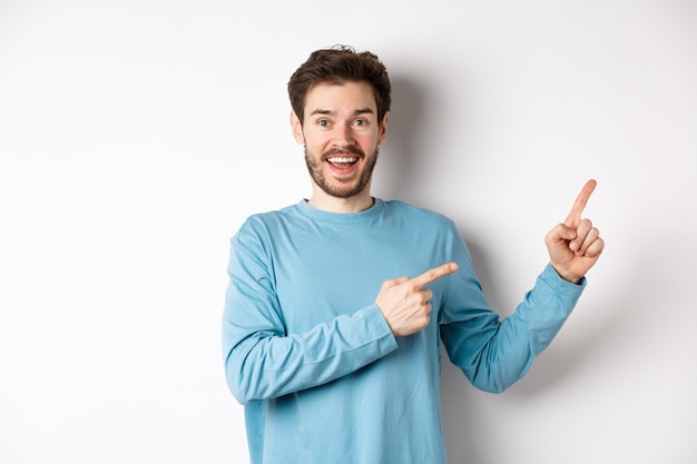 Homme souriant gai pointant les doigts vers la droite et montrant une bannière ou un logo sur un espace blanc pour les publicités, recommandant le produit, debout sur fond de studio