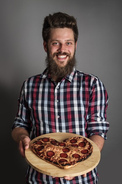 Photo un homme souriant heureux donne une pizza aux formes de coeur brûlé