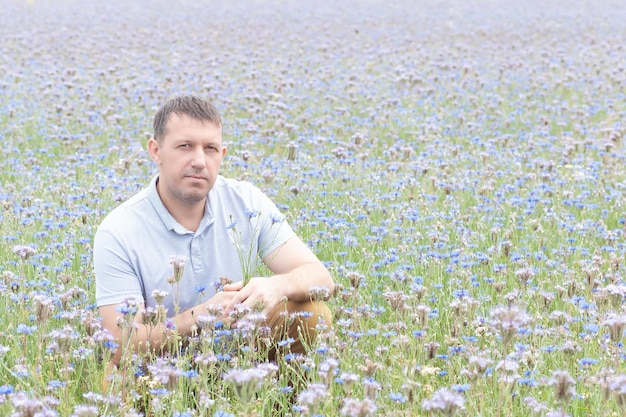 Un homme souriant heureux est assis dans un champ de fleurs de prairie Bonheur et joie