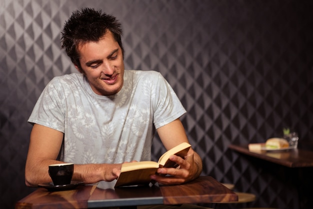 Homme souriant hipster lisant tout en buvant du café