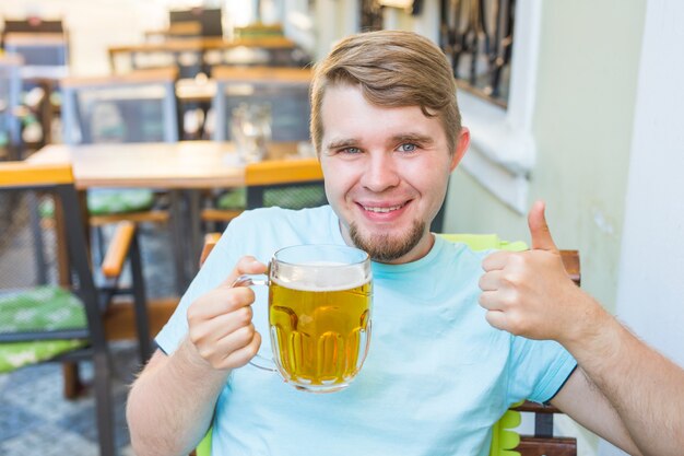 Homme souriant joyeux tenant une grande chope de bière et montrant les pouces vers le haut en plein air