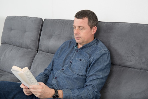 Homme souriant lisant un livre et se relaxant sur un canapé