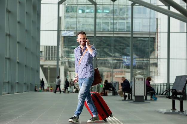 Homme souriant, marchant dans la gare avec un téléphone