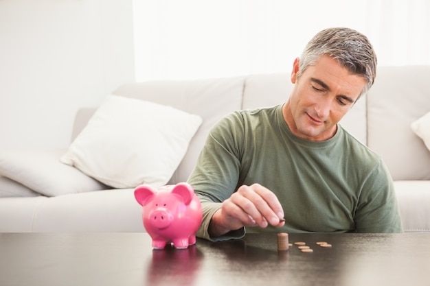 Homme souriant, mettre des pièces de monnaie dans une tirelire