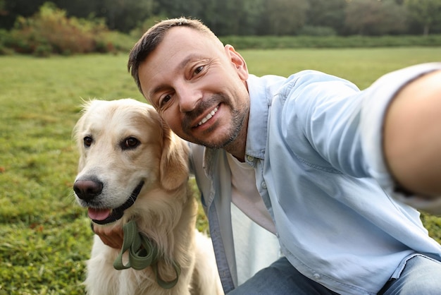 Un homme souriant avec un mignon Golden Retriever prenant un selfie le jour du printemps