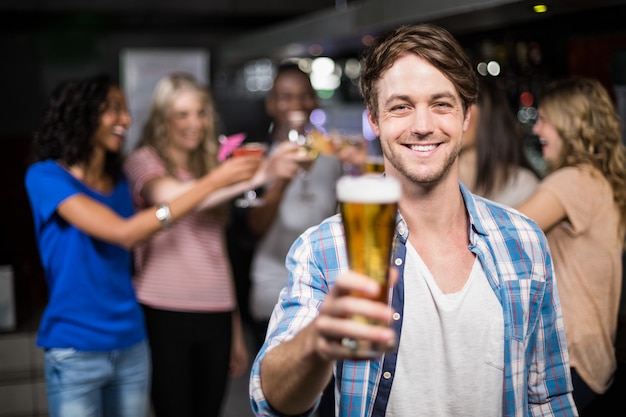 Homme souriant montrant une bière avec ses amis