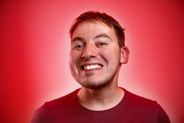 Homme souriant sur un mur rouge.