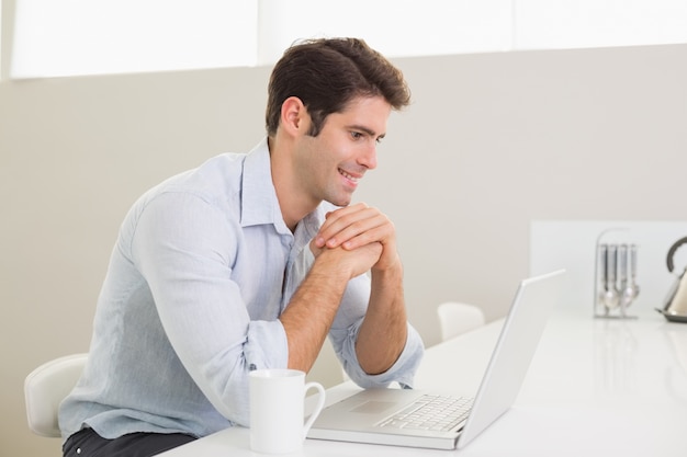 Homme souriant occasionnel à l&#39;aide d&#39;ordinateur portable à la maison