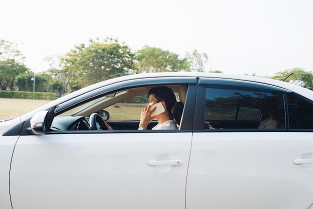 Un homme souriant parle sur un téléphone intelligent dans une voiture blanche. L'homme d'affaires a réussi à conduire sa voiture et à parler au téléphone portable.