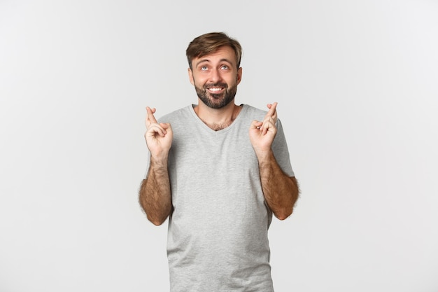 Homme souriant plein d'espoir en t-shirt gris, levant les yeux et faisant voeu