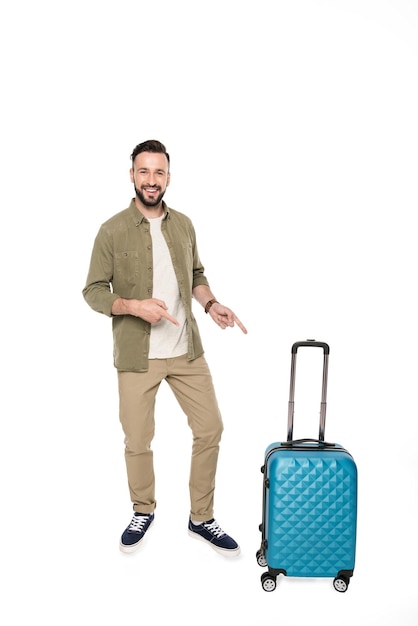 Homme souriant pointant sur la valise et regardant la caméra isolée sur blanc