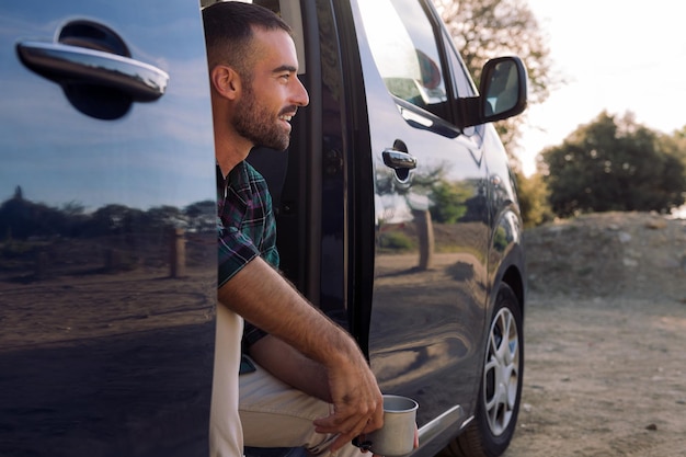 Homme souriant à la porte d'un camping-car avec une tasse