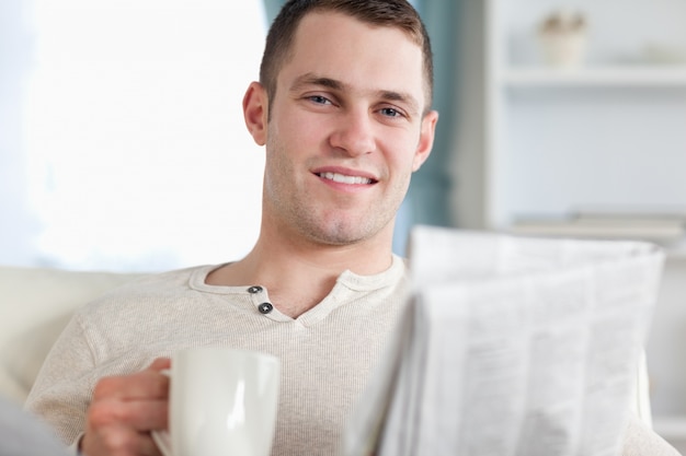 Homme souriant, prenant un thé en lisant les nouvelles