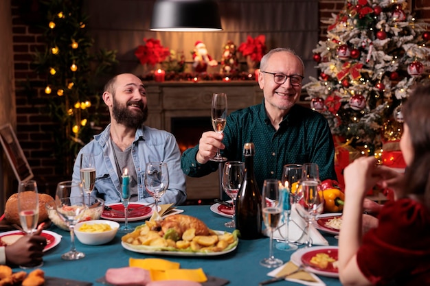 Homme souriant proposant des toasts de noël lors d'un dîner festif, tenant un verre de vin mousseux lors d'un festin à la maison de noël. Famille célébrant les vacances d'hiver, buvant à la fête du nouvel an