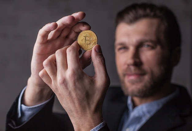 Un homme souriant regarde le bitcoin dans ses mains. Focus sur la pièce