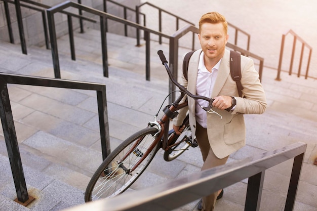 Homme souriant séduisant portant son vélo et regardant au loin