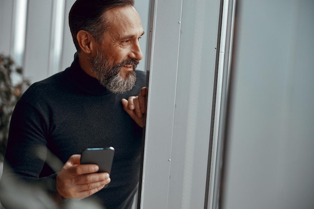 Homme souriant avec téléphone regardant par la fenêtre