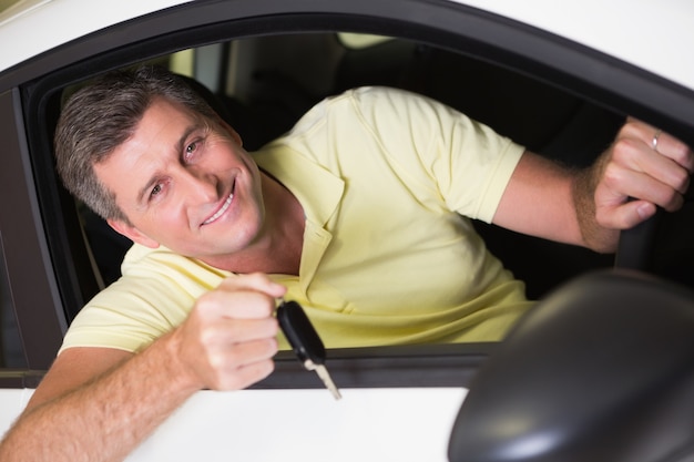Homme souriant, tenant une clé de voiture, assis dans sa voiture