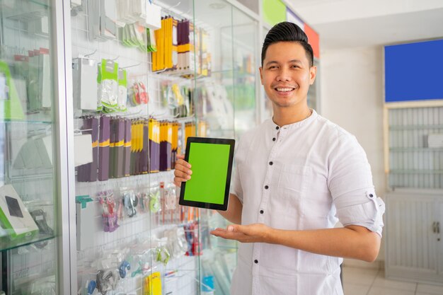 Homme souriant tenant une tablette avec un geste de la main pointant sur l'écran de la tablette près de la vitrine en verre