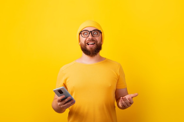 Homme souriant tenant le téléphone sur le concept de gagnant de fond jaune