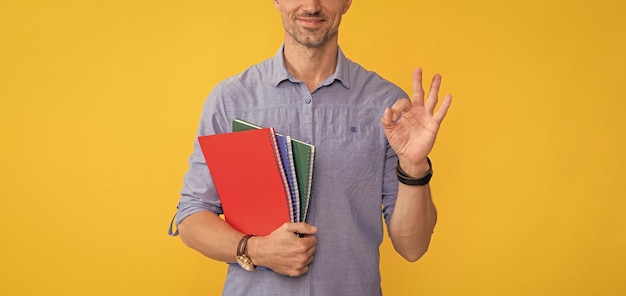 Un homme souriant tient un cahier d'école ou un planificateur montre une école de geste ok