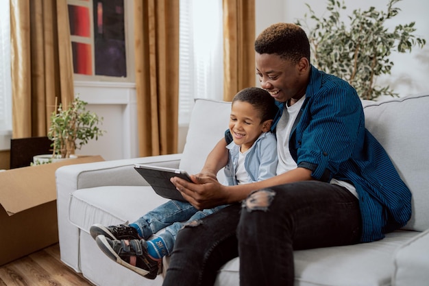 Un homme souriant tient une tablette dans sa main montre à son fils des vidéos d'images drôles qu'ils parcourent